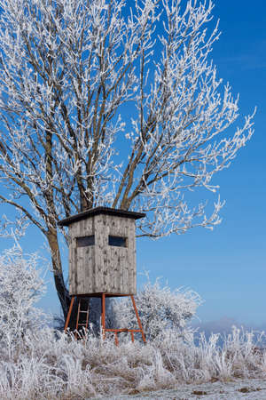 Wooden lookout tower for hunting in winter landscape with frozen trees and blue skyの写真素材