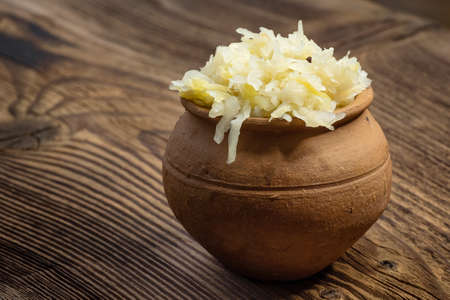 Homemade pickled sauerkraut in a ceramic jar on a wooden board