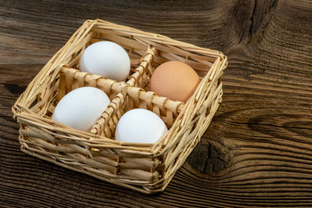 Hen Eggs in a wicker basket on an old vintage planked wood table. Rural kitchen still life. Preparation for Easter.の写真素材