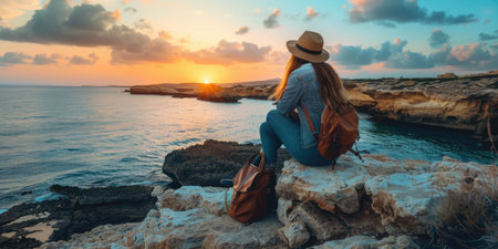 Serene image of a woman in a summer outfit sitting and watching a beautiful sunset over the seaの素材
