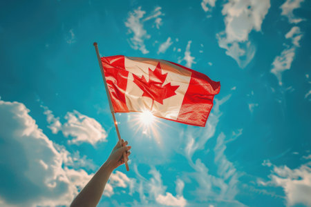 Human hand arm waving Canadian flag against blue sky. Celebrating national Canada Dayの素材