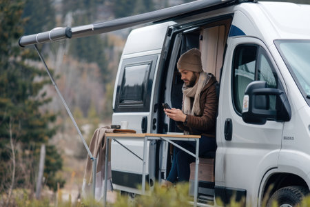 Digital nomad using smartphone while working remotely from his camper van, enjoying freedom and natureの素材