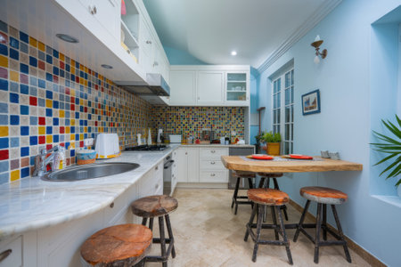Stylish kitchen featuring vibrant mosaic tiles, white cabinets, and a charming wooden dining area, creating a cozy and inviting atmosphereの素材
