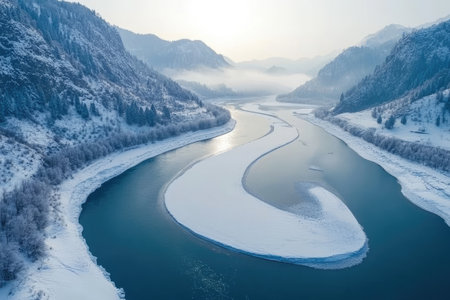 Aerial view of a frozen river winding through snow covered mountains on a cold winter dayの素材