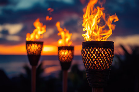 Flames flicker in tiki torches at sunset creating a warm and inviting ambiance on a tropical beachの素材