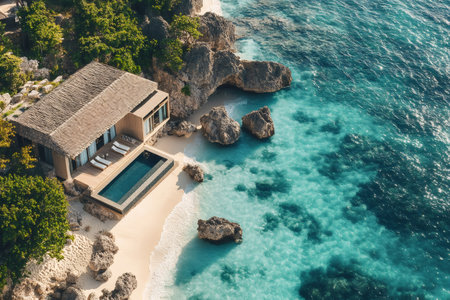 Breathtaking aerial view of a luxurious beach house with infinity pool nestled on a secluded cove, surrounded by lush vegetation and crystal-clear turquoise watersの素材