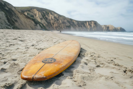 Wooden surfboard lying on a beach with cliffs and ocean waves creating a summer surfing vibeの素材