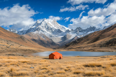 Stunning mountain landscape with a bright orange tent pitched by a serene lake, offering breathtaking views of the snow-capped peaksの素材