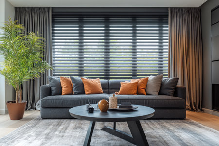 Stylish and cozy living room with a gray sofa, orange cushions, and a modern coffee table, featuring large windows with blinds and curtainsの素材