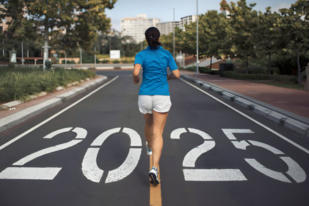 Sportswoman running on a city street towards the 2025 writing on the asphalt, symbolizing goals, future, and new year's resolutionsの素材