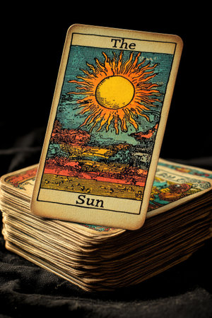 The sun tarot card is laying on top of a deck of cards, showing a bright yellow sun with the words the sun printed belowの素材