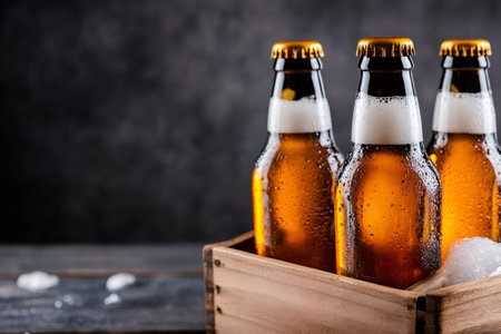 Ice cold beer bottles with condensation in a wooden crate on a table against a dark backgroundの素材