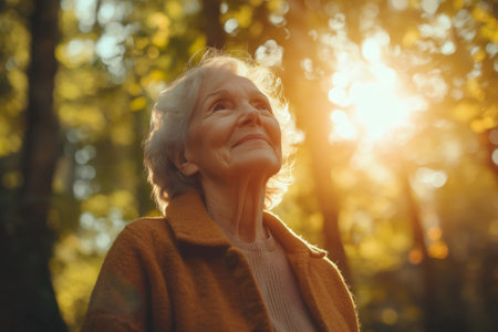 Senior woman looking up at sunlight while enjoying a walk in a colorful autumn forestの素材