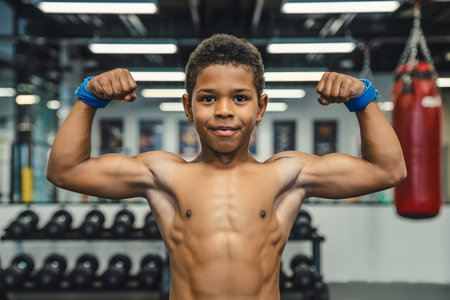 Strong boy flexing biceps in a gym, demonstrating the results of his hard work and dedication to fitnessの素材