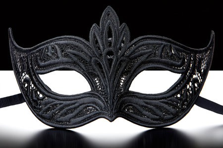 Intricate black lace mask with decorative embellishments, placed on a reflective surface against a dark background, creating a sense of mystery and eleganceの素材