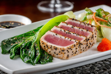 Sesame crusted seared tuna with bok choy, dipping sauce, and garnish, served on a white rectangular plateの素材