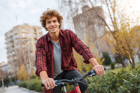 Happy young man enjoying a leisurely bike ride through a vibrant urban park during the colorful autumn seasonの素材