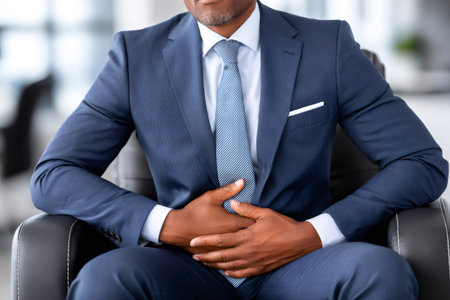 Businessman experiencing stomach or abdominal pain, possibly from indigestion or other digestive issues, while sitting in an office chairの素材