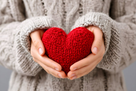 Woman wearing a knitted sweater is holding a red knitted heart, symbolizing love, care, and warmthの素材
