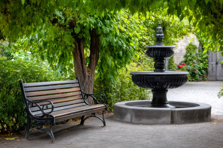 Peaceful garden scene featuring a wooden bench and a two-tiered fountain, creating a serene atmosphereの素材