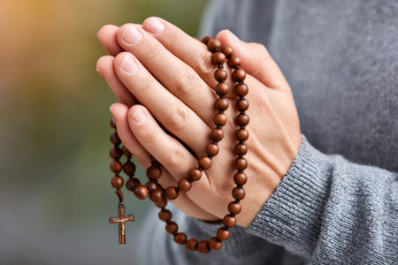Woman praying with wooden rosary beads in clasped hands, offering a moment of reflection and spiritualityの素材