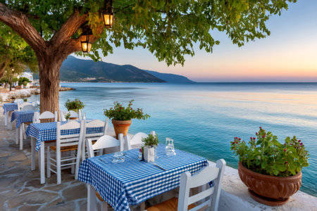 White tables with blue checkered tablecloths under a tree by the sea at sunset are waiting for customers in a greek restaurantの素材