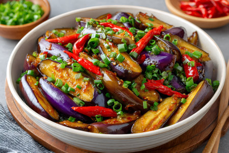 Sizzling yu xiang qie zi, a flavorful dish of stir fried eggplant with garlic, chili peppers, and scallions, served in a bowlの素材