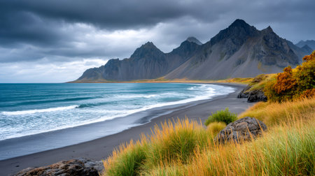 Panoramic view of waves meeting reynisfjara black sand beach with vestrahorn mountains under a cloudy skyの素材