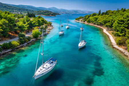 Sailboats anchored in a calm bay with clear turquoise water and green coastlineの素材