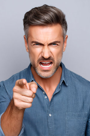 Frowning man with gray hair screaming and pointing aggressively at the viewer, showing rageの素材