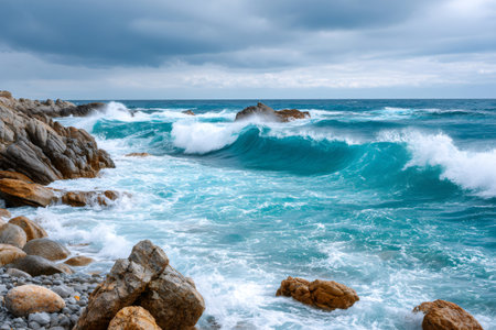 Dynamic blue ocean waves breaking on a rugged coastline under a cloudy skyの素材