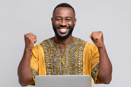 Happy african man in traditional clothes celebrating victory with clenched fistsの素材