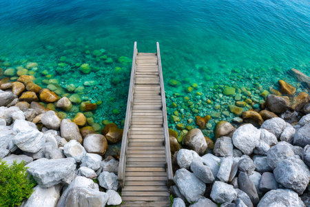 Wooden pier extending into clear turquoise water with an underwater rocky bottom and rocky shoreの素材