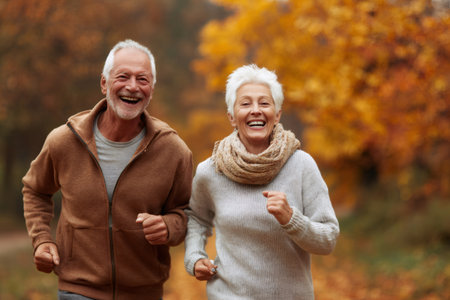 Happy elderly couple jogging, enjoying an active lifestyle in a fall parkの素材