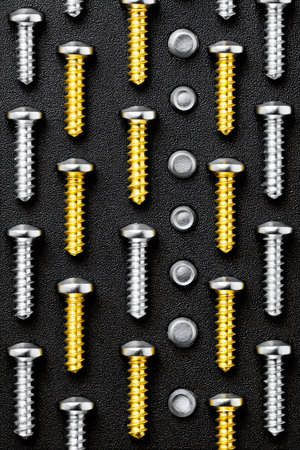 Metallic screws and nuts arranged in a grid pattern on a black textured surfaceの素材
