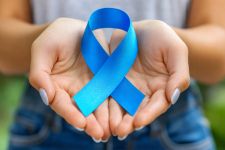Hands cupping a blue ribbon, symbolizing health awareness and supportの素材