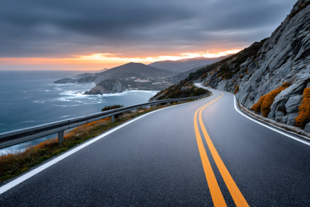 Winding highway following the coastline with an ocean sunset and rugged cliffsの素材