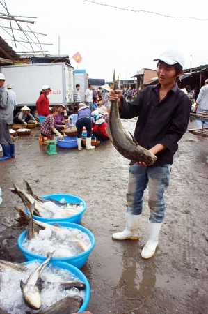 The young man wear boot hole big fish with funny face at crowded, marshy fishing market in vertical frame  July 15, 2013のeditorial素材