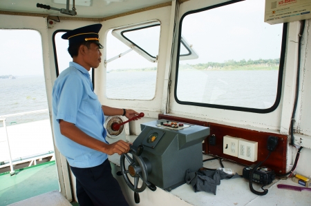 On cabin of ferry boat, ferryman wear uniform control the wheel to transportation passenger cross the river. Take with color, horizontal frame at Dong Thap, January 27, 2013のeditorial素材