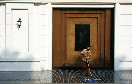 HO CHI MINH CITY, VIETNAM- MAY 12  Young man working on five star hotel lobby, he wear employee uniform, cleaning tile floor, luxury hotel with white wall, wooden door, Saigon, Viet Nam, May 12, 2014のeditorial素材