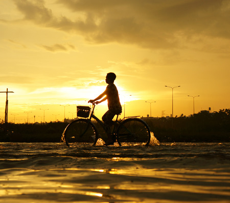 HO CHI MINH CITY, VIET NAM- OCT 9: Amazing scene of Ho Chi Minh city when flood tide, street flooded, silhouette of people riding motorbike, bike in water at sunset, yellow sun, Vietnam, Oct 9, 2014のeditorial素材