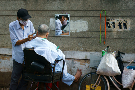 HO CHI MINH, VIET NAM- OCT10: Traditional lifestyle of poor people in Asia urban, Vietnamese male barber work at open air shop on pavement, man cut hair for senior to make living, Vietnam, Oct10, 2014のeditorial素材