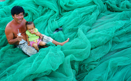 PHAN RANG, VIET NAM- OCT 23: Asian grandfather carry kid, sitting on fishing net at Vietnamese fishing village, happy family with old and young people,  smile face on cyan color, Vietnam, Oct 23, 2014のeditorial素材