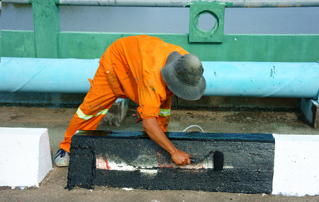 Asian worker working on street, Vietnamese man painting traffic paint on asphalt road, male wear orange work wear, working on day,Ho chi Minh city, Vietnamのeditorial素材
