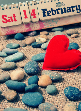 Red heart, symbol of love with desk calendar, Feb 14 on it, nice pebble, fiber  background, with vintage color, Valentine day is special day for lover with sweetheartの写真素材