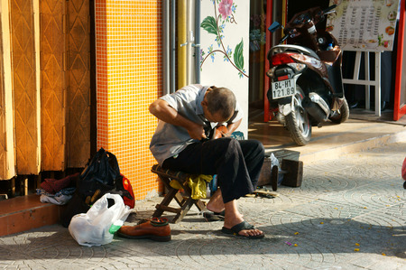 HO CHI MINH CITY, VIET NAM- FEB 6: Senior Vietnamese man working for living on sidewalk, he sitting, repair shoes for customer, many poor people earning money by this trade, Vietnam, Feb 6, 2015のeditorial素材