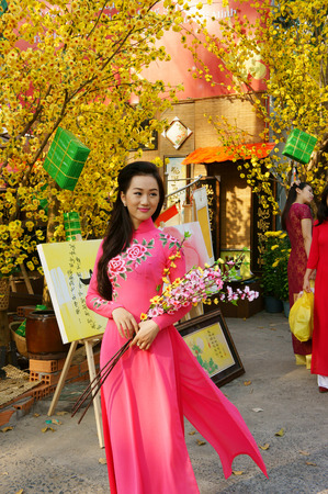 HO CHI MINH CITY, VIET NAM- FEB 7: Atmosphere of springtime with colorful scene on Saigon street, Vietnamese woman in ao dai, posing beside flower to take photo on Tet holiday, Vietnam, Feb 7, 2015のeditorial素材