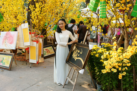 HO CHI MINH CITY, VIET NAM- FEB 7: Atmosphere of springtime with colorful scene on Saigon street, Vietnamese woman in ao dai, posing beside flower to take photo on Tet holiday, Vietnam, Feb 7, 2015のeditorial素材