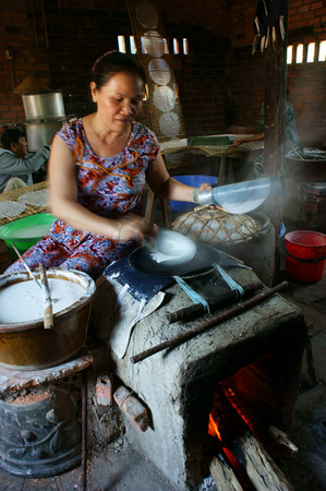 BA RIA, VIET NAM- FEB 11: Asian woman sitting, working at home, Vietnamese female make rice paper from rice flour at banh trang trade village, smoke from firewood cooker, Vietnam, Feb 11, 2015のeditorial素材