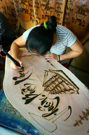 QUY NHON, VIET NAM- AUG 23: Vietnamese artist doing wood engraving by fire pen, man engrave Han Mac Tu poem at souveir shop of Genh Rang tourist area, a famous poet, Quynhon, Vietnam, Aug 23, 2015のeditorial素材